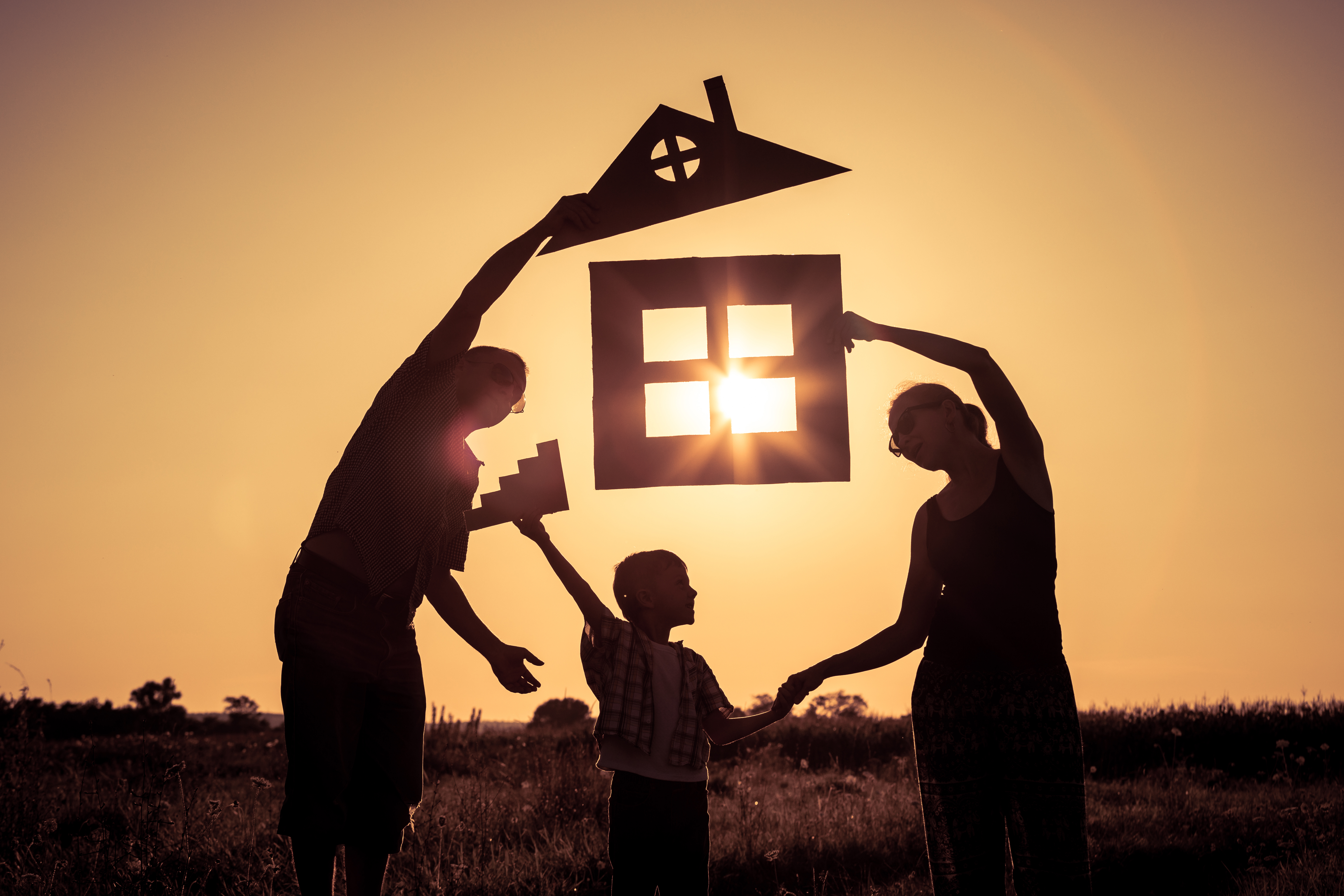 Happy family standing on the field at the sunset time. They buil